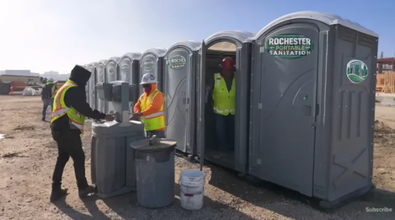 Workers in safety vests at a row of Rochester Portable Sanitation porta potties and a hand wash station on a job site