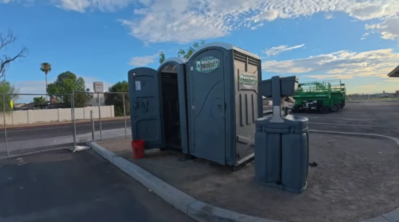 Standard porta potties and a hand wash station placed beside a parking lot