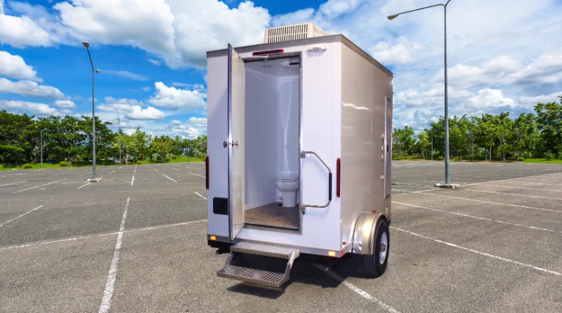 Restroom trailer with open door and entry step parked on a paved lot