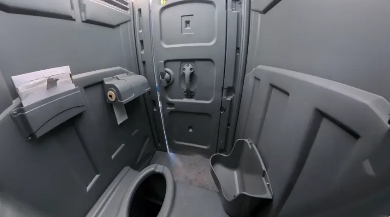 Inside a standard porta potty in Rochester, NY showing the toilet seat, toilet paper roll and waste bin